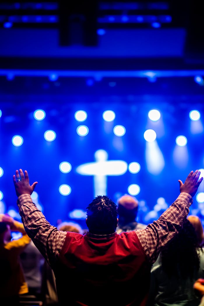 Crowd gathered in worship with a focus on a cross and dynamic stage lighting.